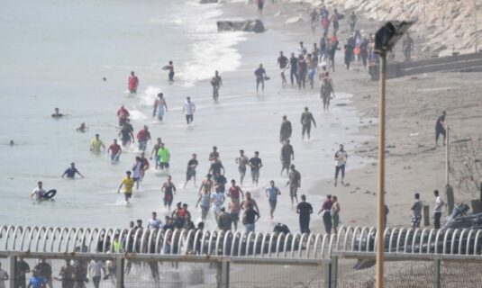 cientos de personas cruzan a nado a ceuta desde marruecos con una multitud esperando al otro lado de la frontera